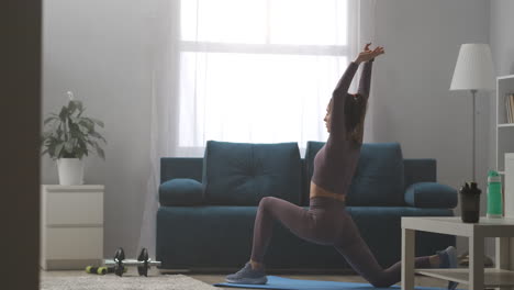 Yoga-Praxis-Zu-Hause.-Eine-Junge,-Sportliche-Frau-Trainiert-Alleine-Im-Wohnzimmer-Und-Führt-Am-Wochenende-Kriegerpose-Dehnübungen-In-Asanas-Durch